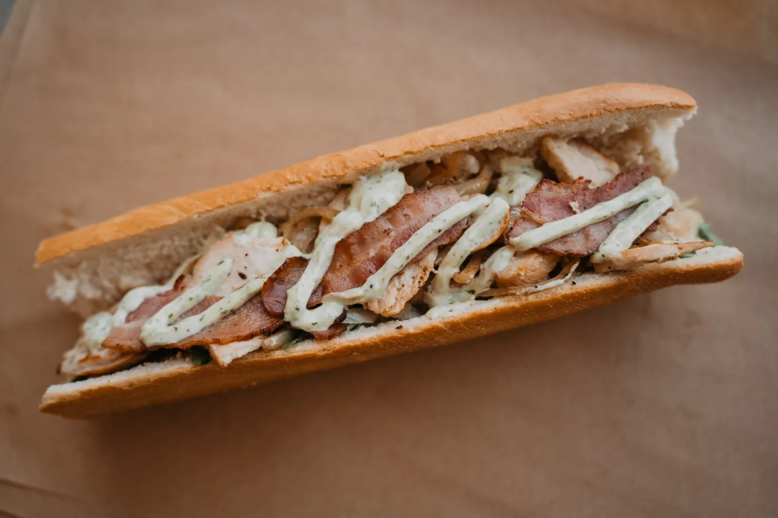 Broodje Chapeau met gegrilde kip, bacon, ui en pestomayonaise op stokbrood